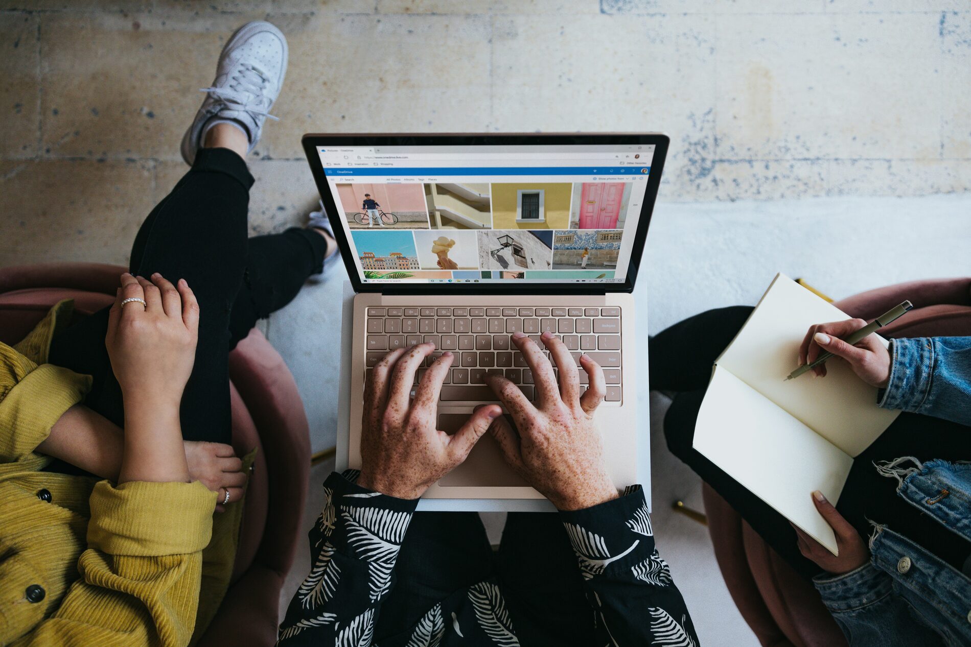 Van bovenaf gefotografeerde laptop met foto's op het scherm, twee mensen werken samen met een notitieboek