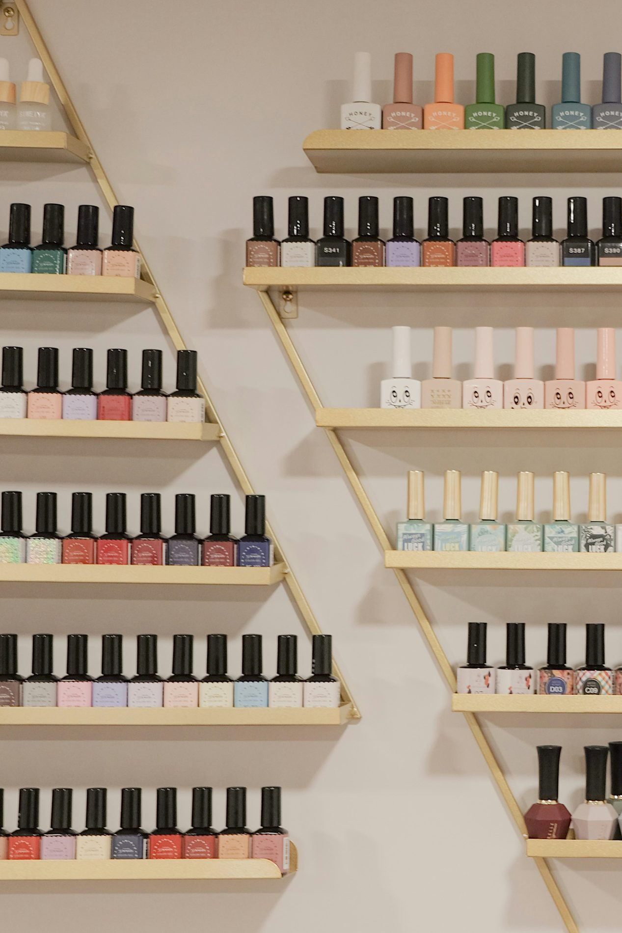 Wand vol flesjes nagellak in tientallen kleuren op houten plankjes in een nagelstudio
