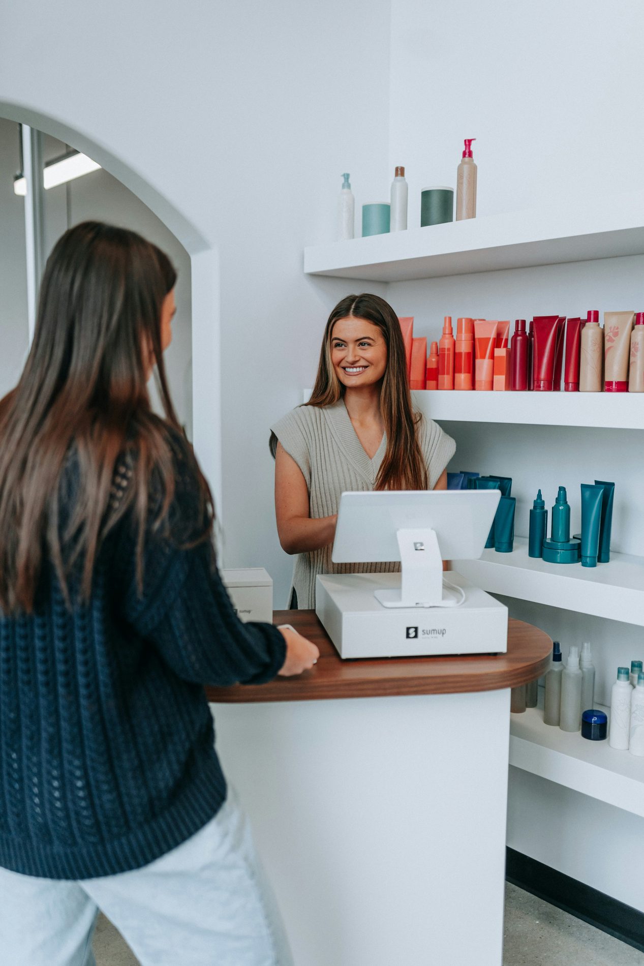 Lachende beauty-ondernemer achter de balie van haar salon, met verzorgingsproducten op de schappen