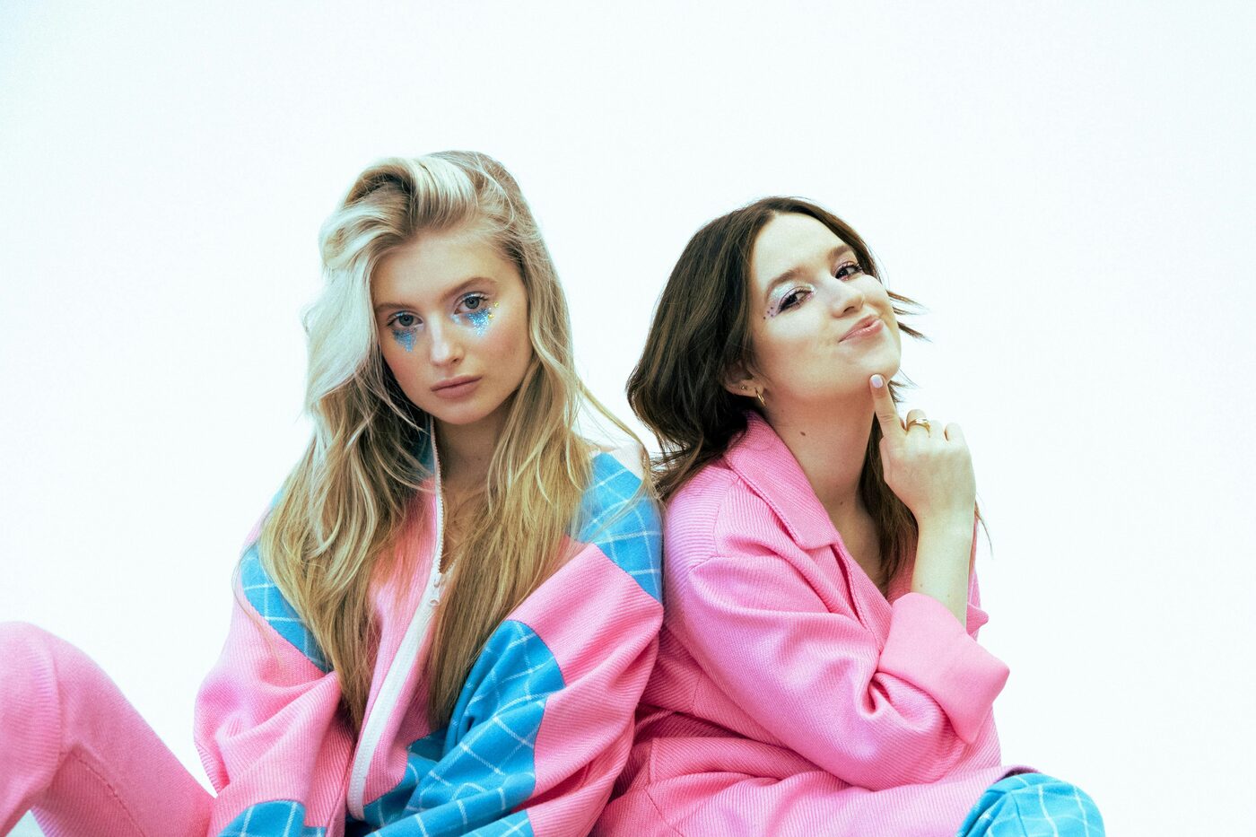 Twee modellen met glitter-make-up poseren speels tegen een lichte achtergrond