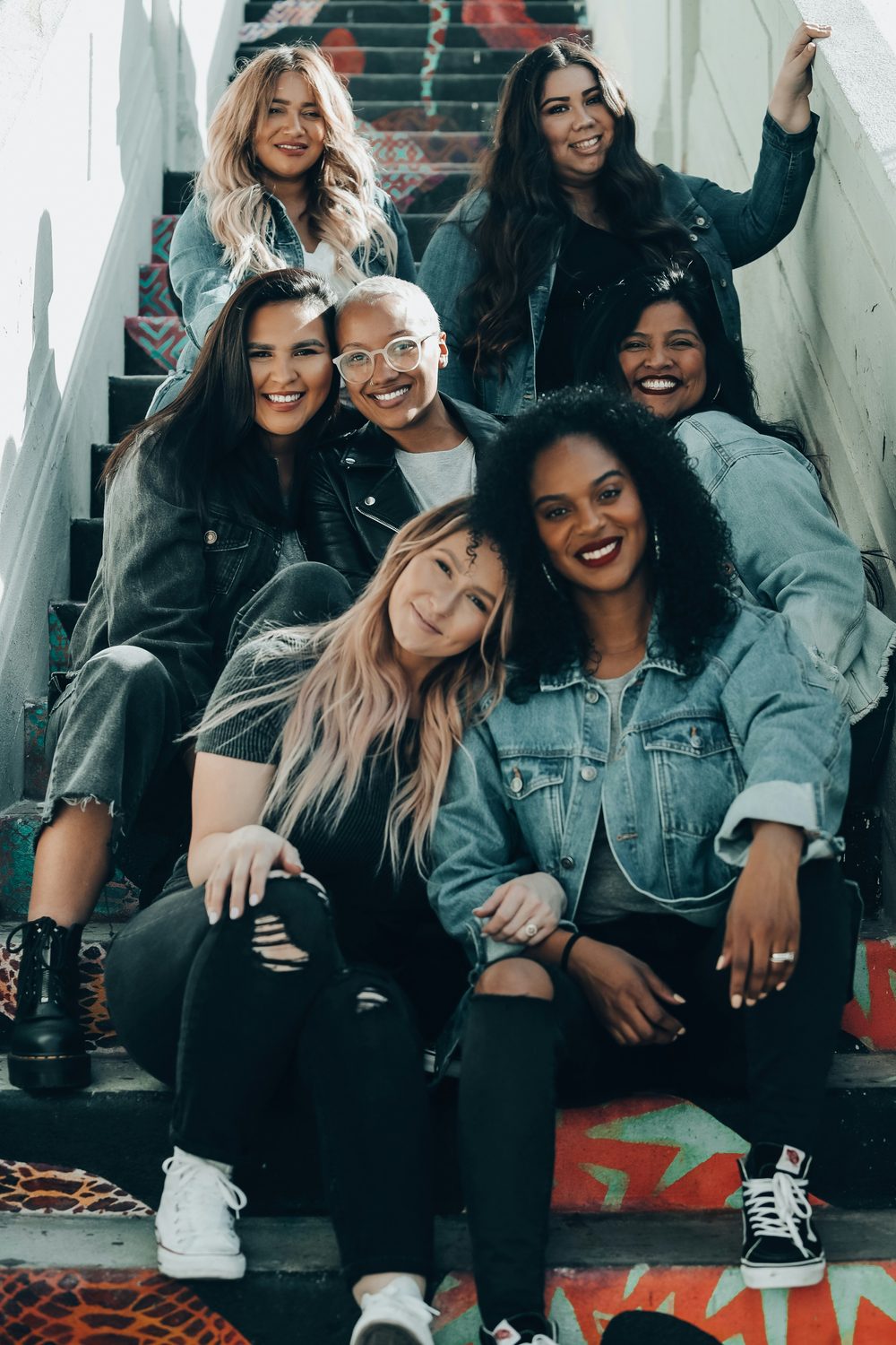 Groep lachende vrouwen samen op een kleurrijke trap, symbool voor de besloten beauty-community