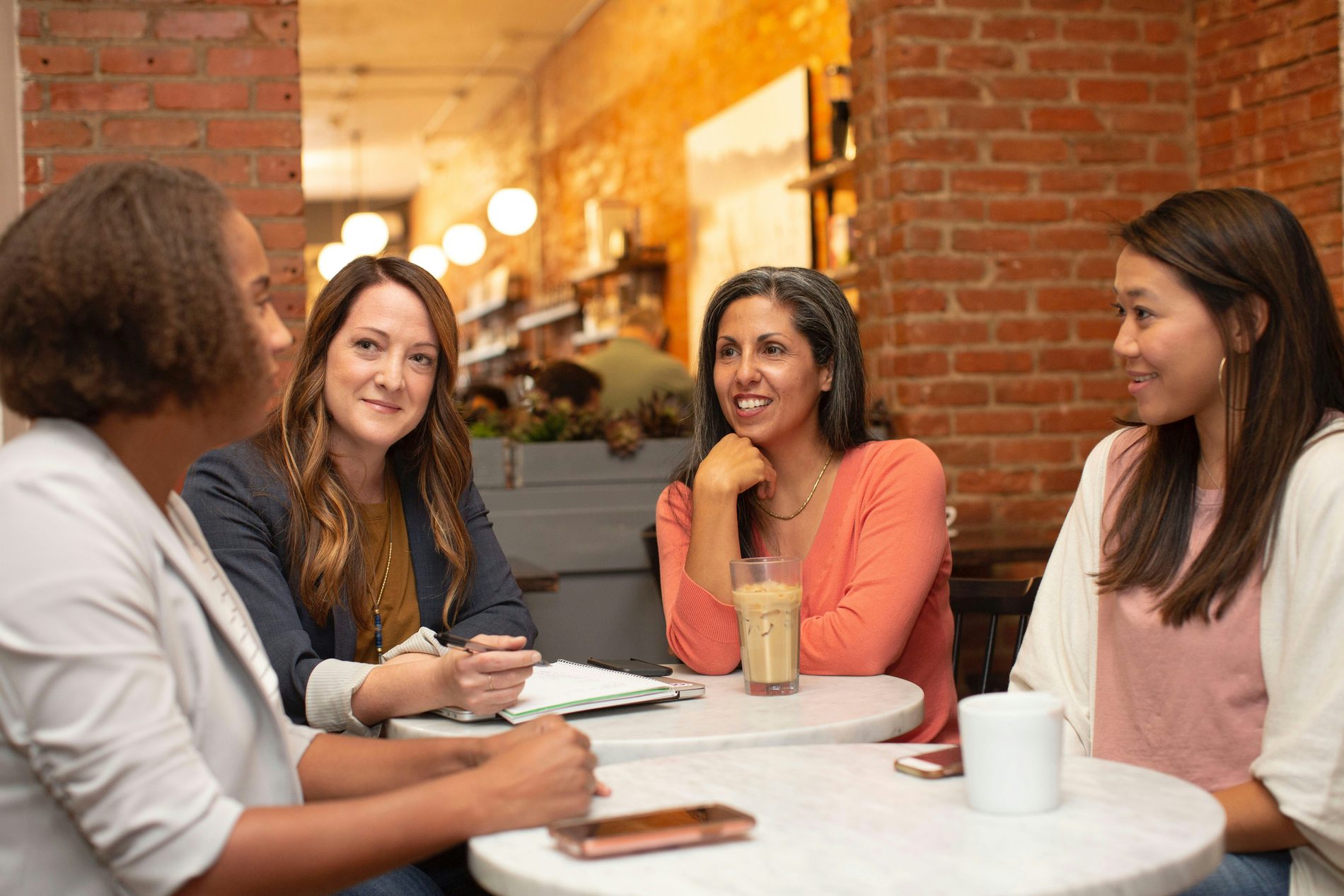 Vier vrouwelijke beauty-ondernemers in gesprek aan een cafetafel met een notitieblok en koffie