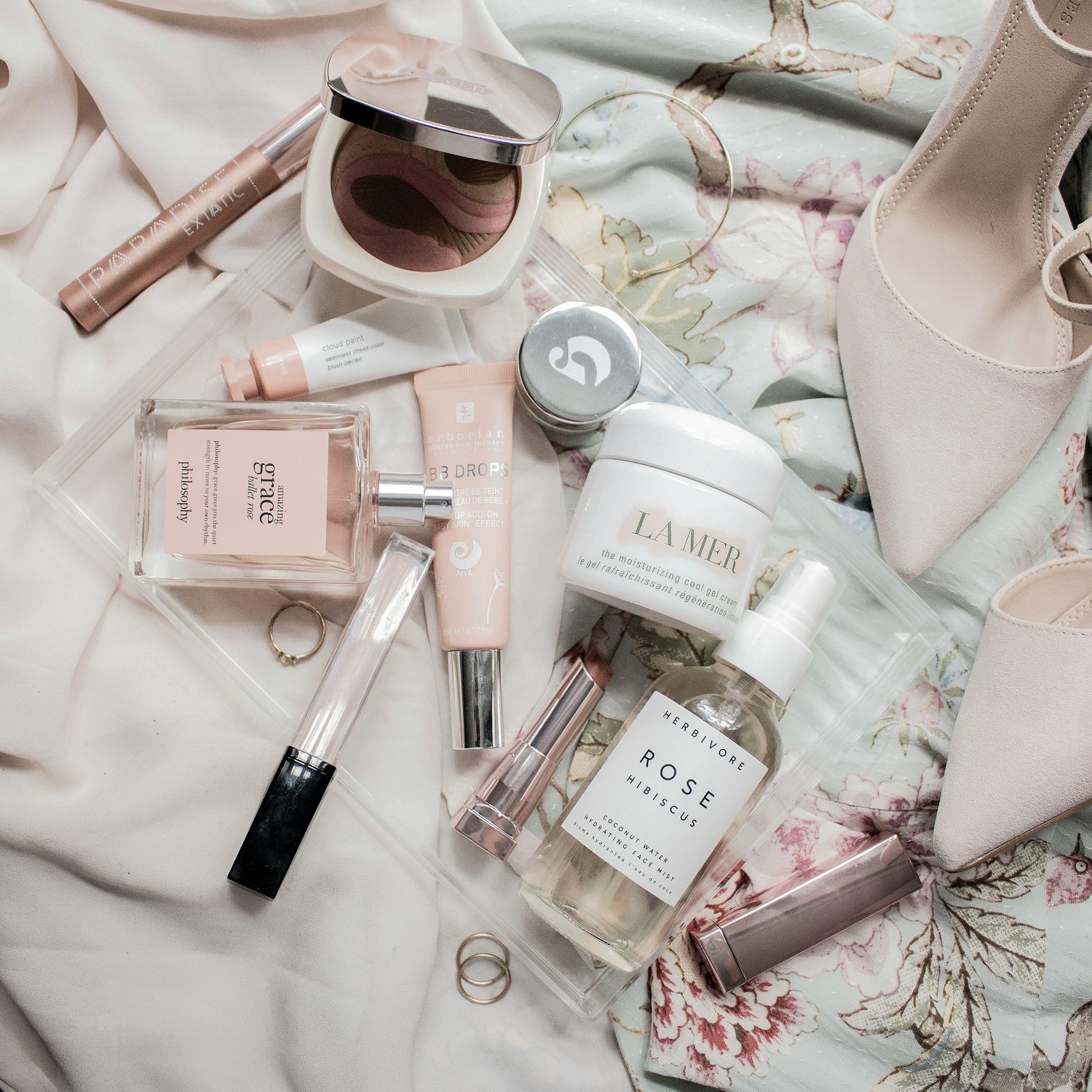 Flatlay van diverse zomer beautyproducten in zachte roze tinten, met een gezichtsmist, dagcreme, blush en parfum
