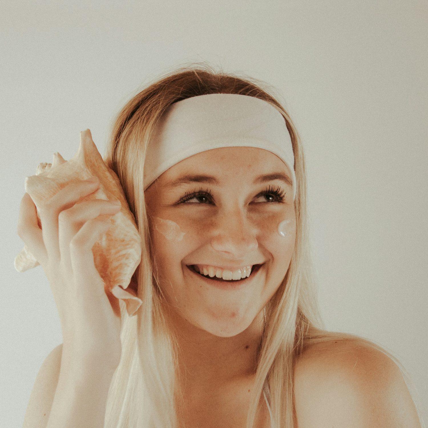 Lachende klant met een haarband en verzorgende creme onder de ogen in een lichte salonruimte