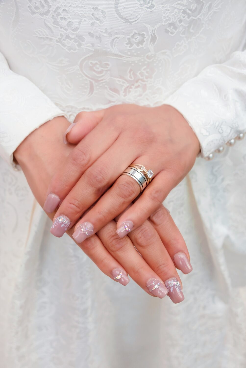 Handen van een bruid met een verzorgde nude manicure met kleine steentjes, over een kanten jurk
