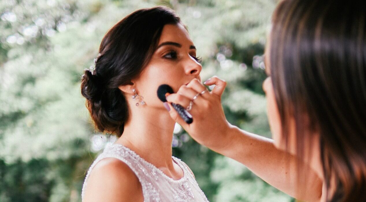 Bruid krijgt de laatste hand aan haar make-up van een visagist, buiten in een groene tuin