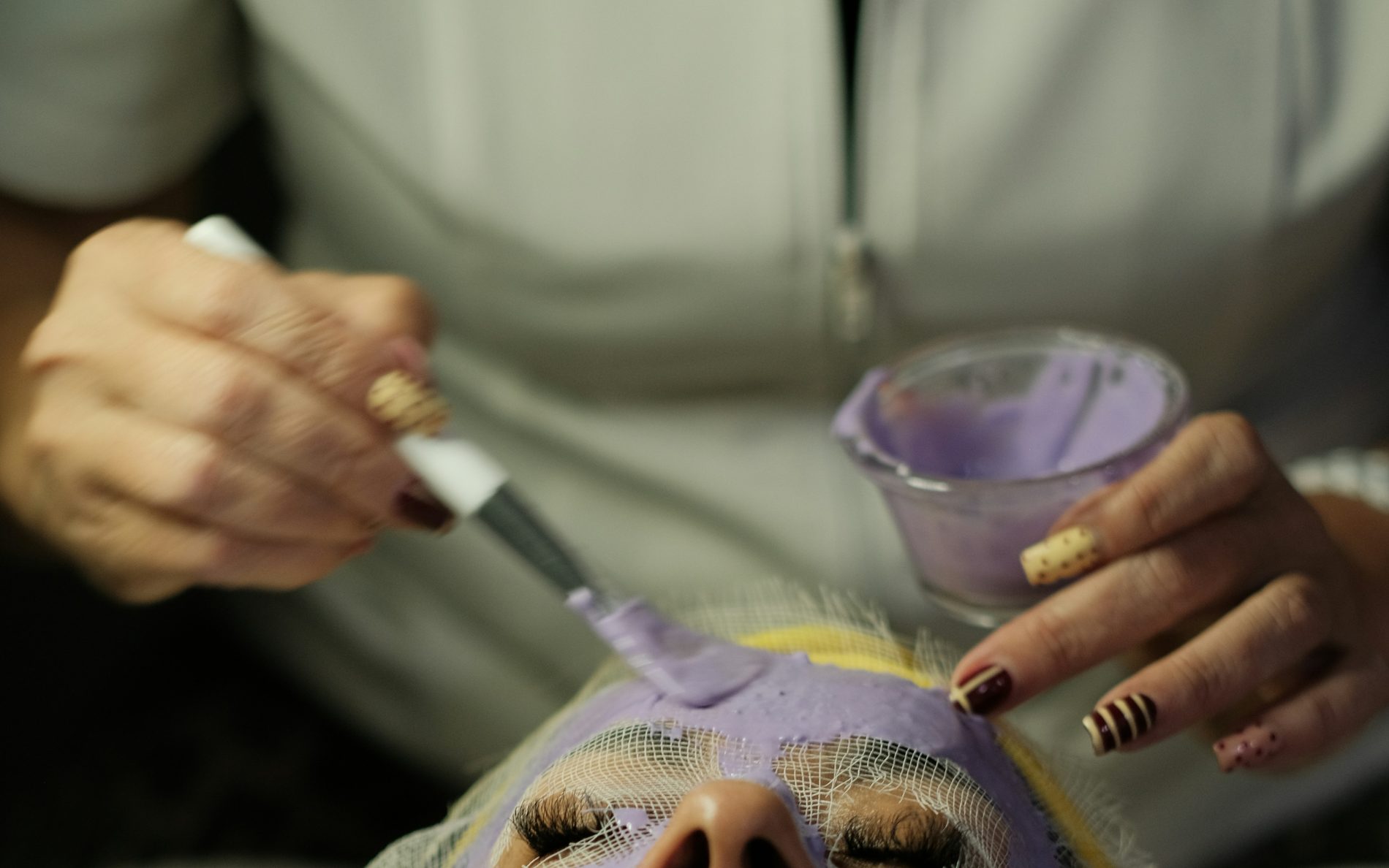 Close-up van een schoonheidsspecialist die met een kwast een gezichtsmasker aanbrengt, met zichtbare techniek en afwerking
