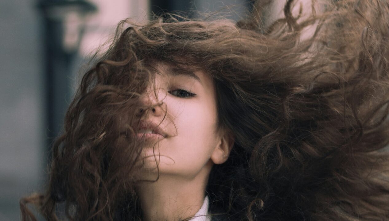 Vrouw met lang, krullend haar dat opwaait in de wind, met zichtbare pluis en volume