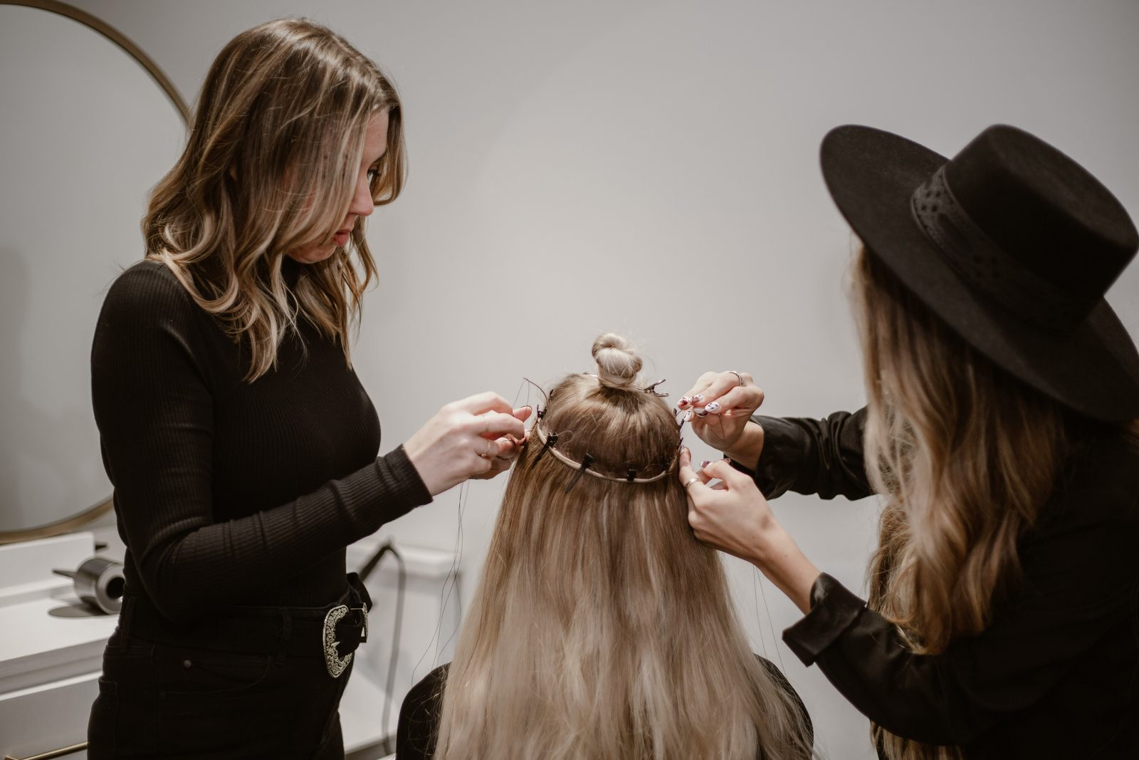 Twee kappers werken samen aan het haar van een klant in een lichte salon