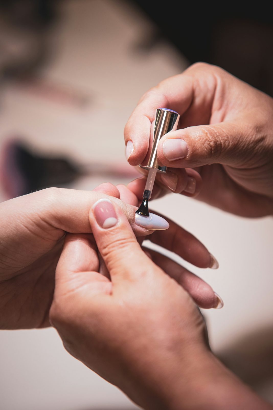 Nagelstyliste brengt een dunne laag gellak aan op de nagel van een klant