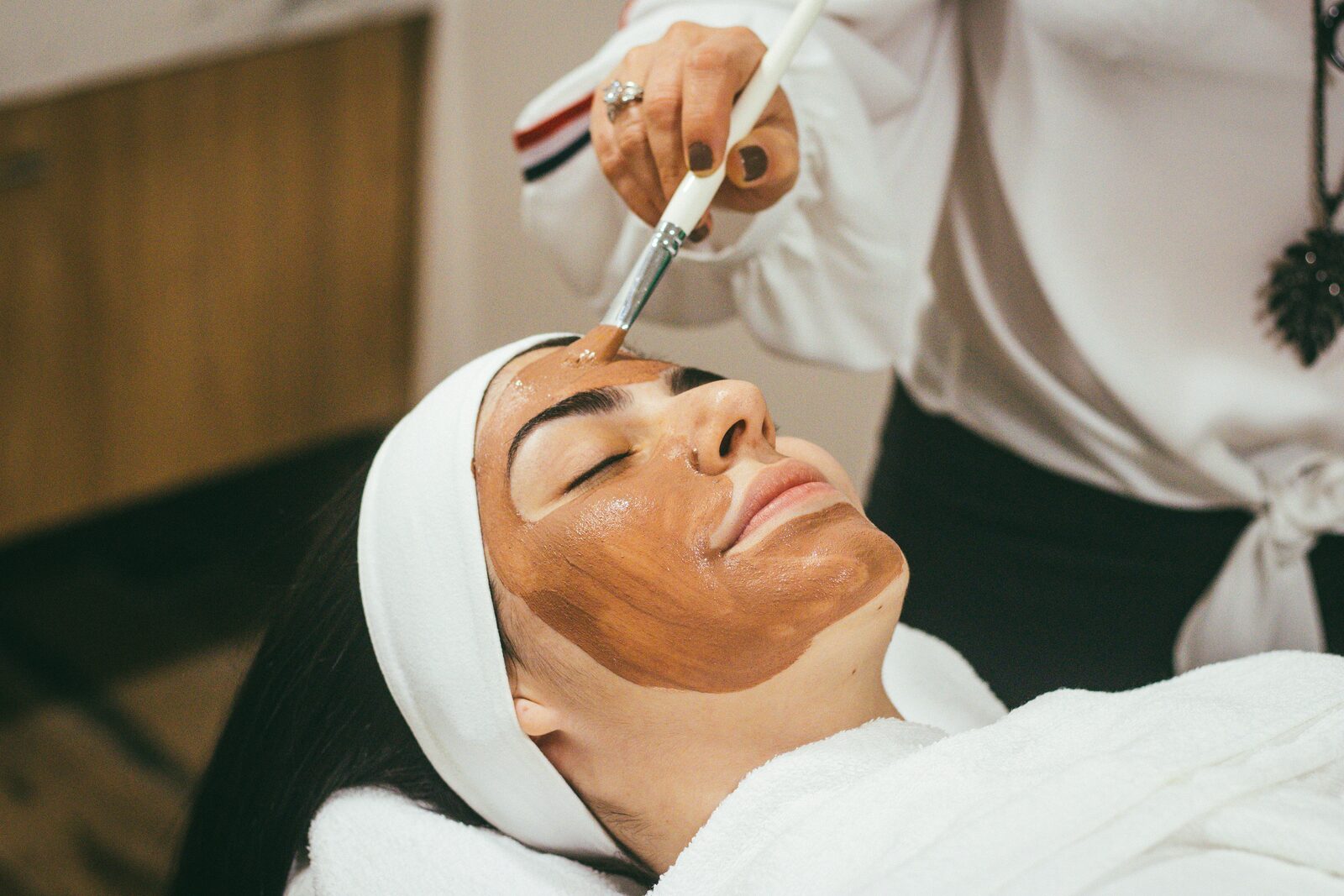 Huidspecialist brengt met een kwast een masker aan tijdens een gezichtsbehandeling