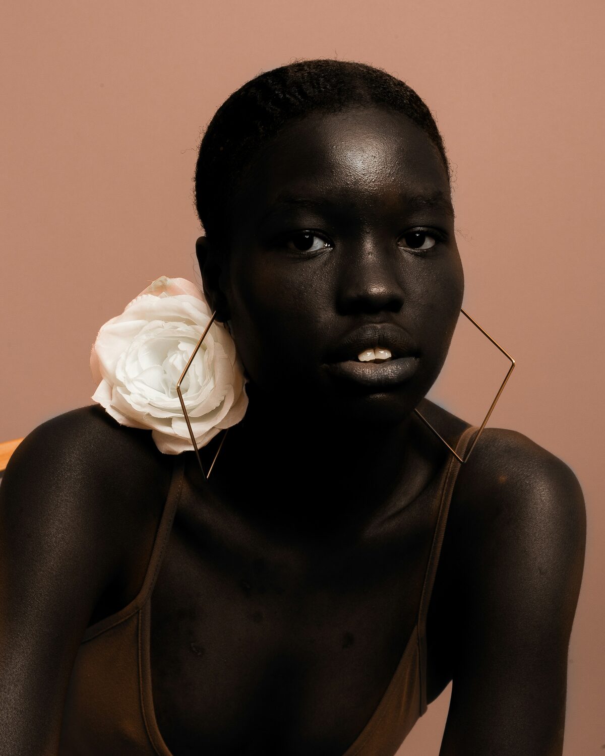 Editorial portret van een vrouw met een witte roos en een grote geometrische oorbel tegen een zachtroze achtergrond