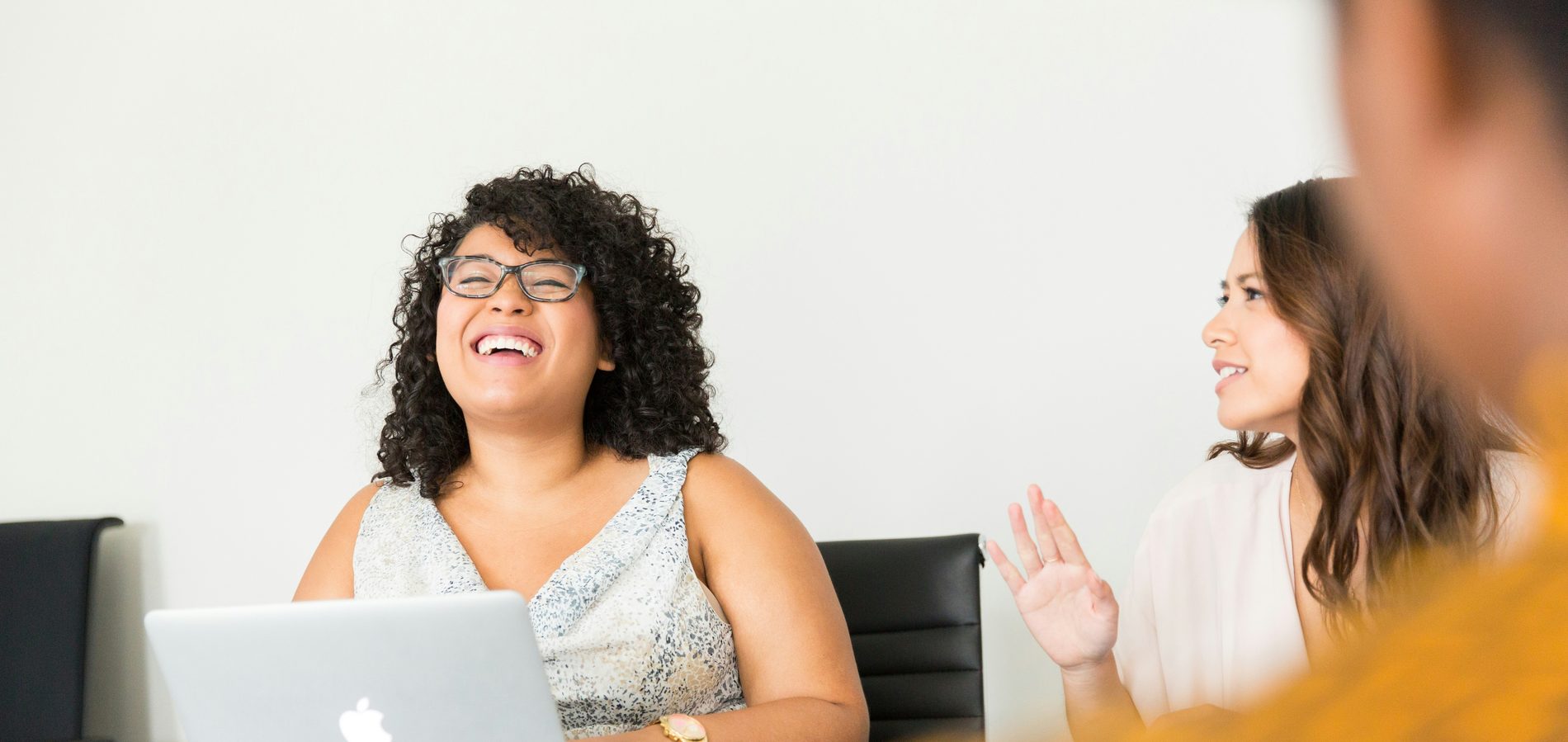 Lachende onderneemster met laptop in overleg met twee anderen aan een vergadertafel