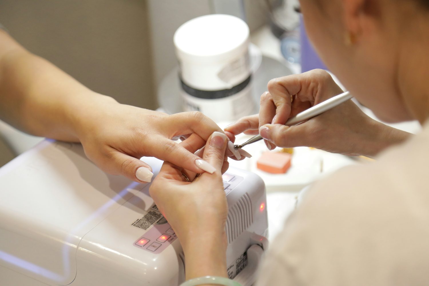 Nagelstyliste werkt de nagelriemen bij tijdens een manicure onder een nageldroger in de studio