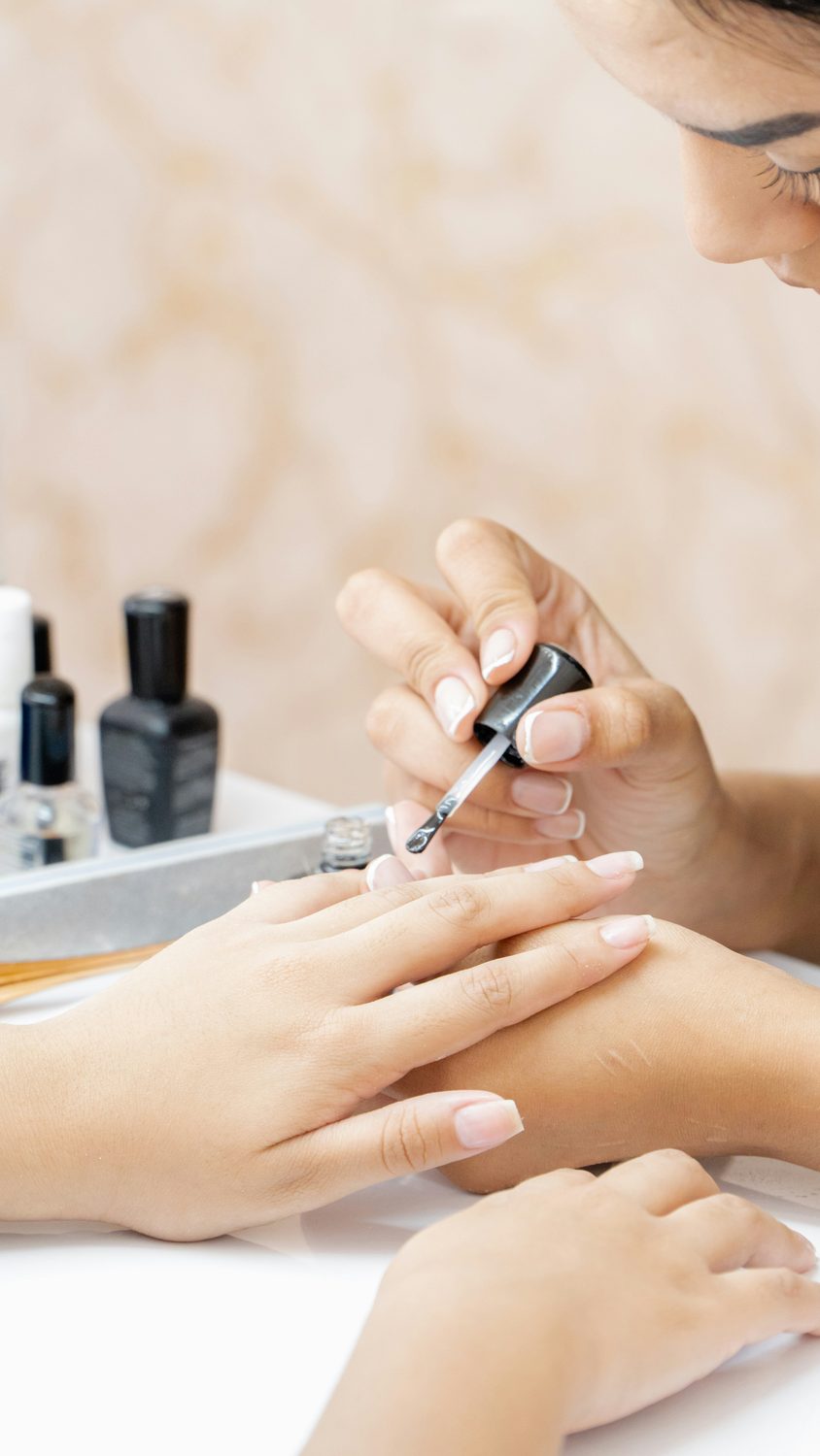Nagelstyliste brengt van dichtbij een laklaag aan op de nagels van een klant tijdens een manicure