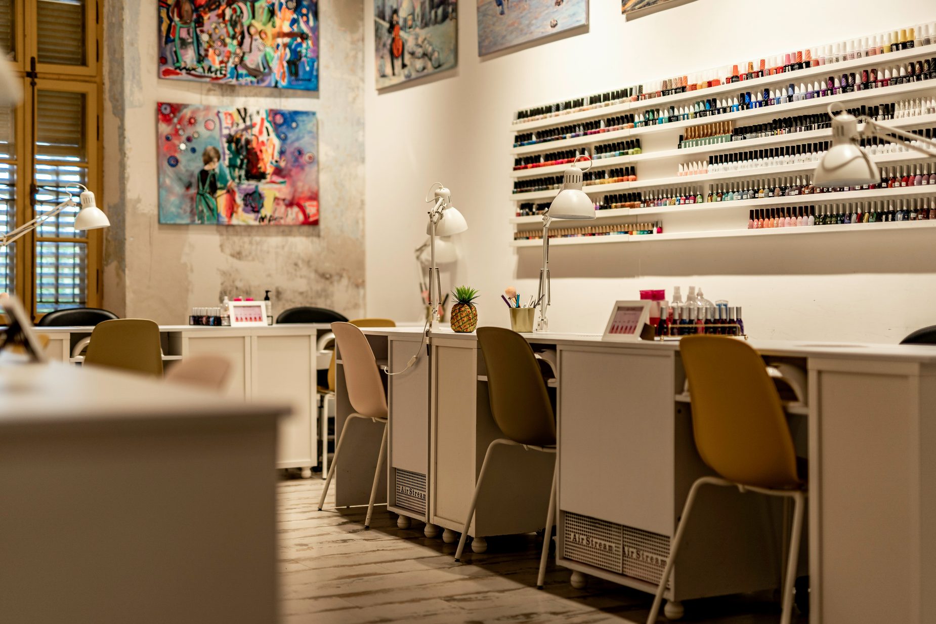 Nagelstudio met manicuretafels, stoelen en een wand vol nagellak in tientallen kleuren
