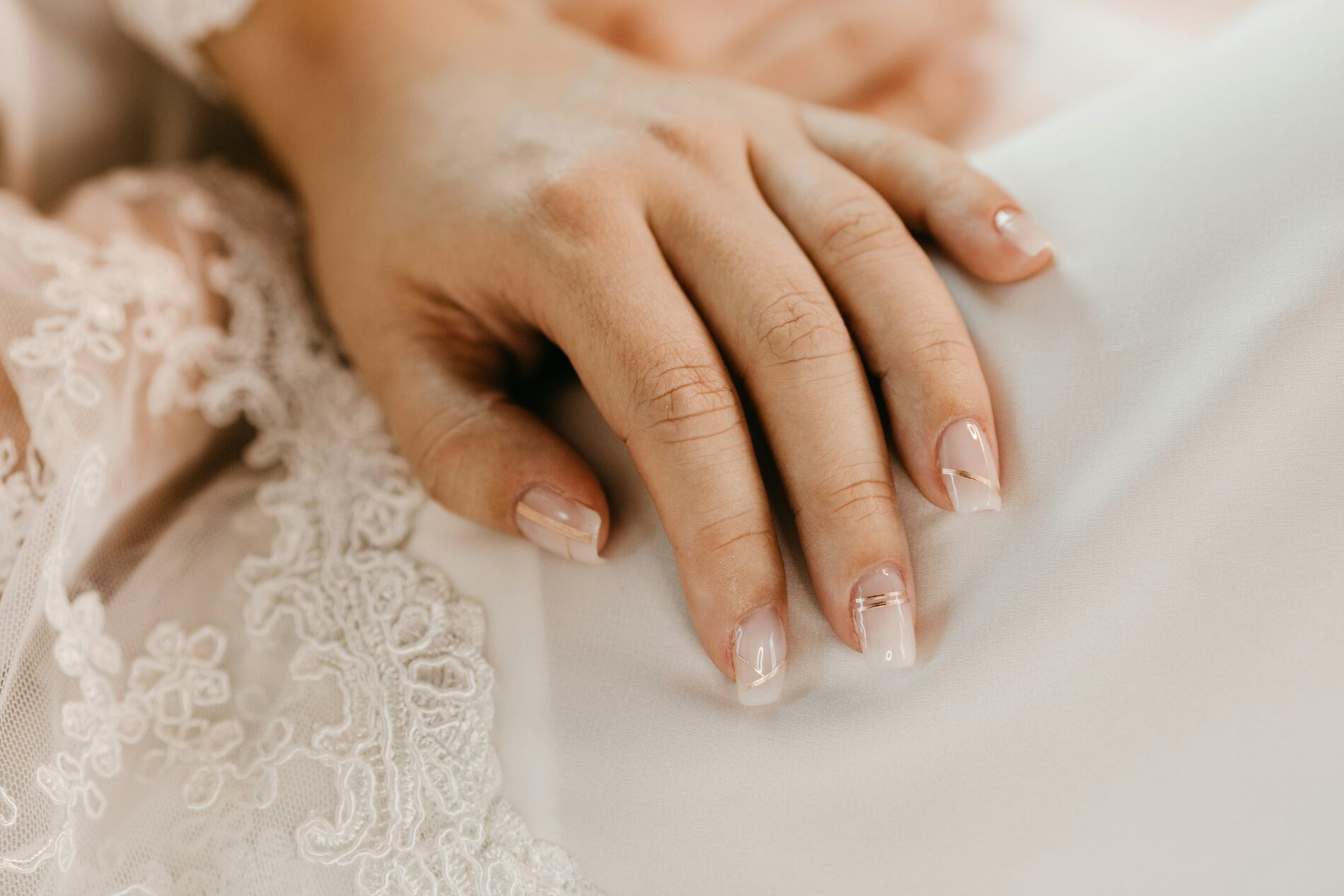 Close-up van een hand met een natuurlijke, glanzende nude manicure en een dun gouden lijntje