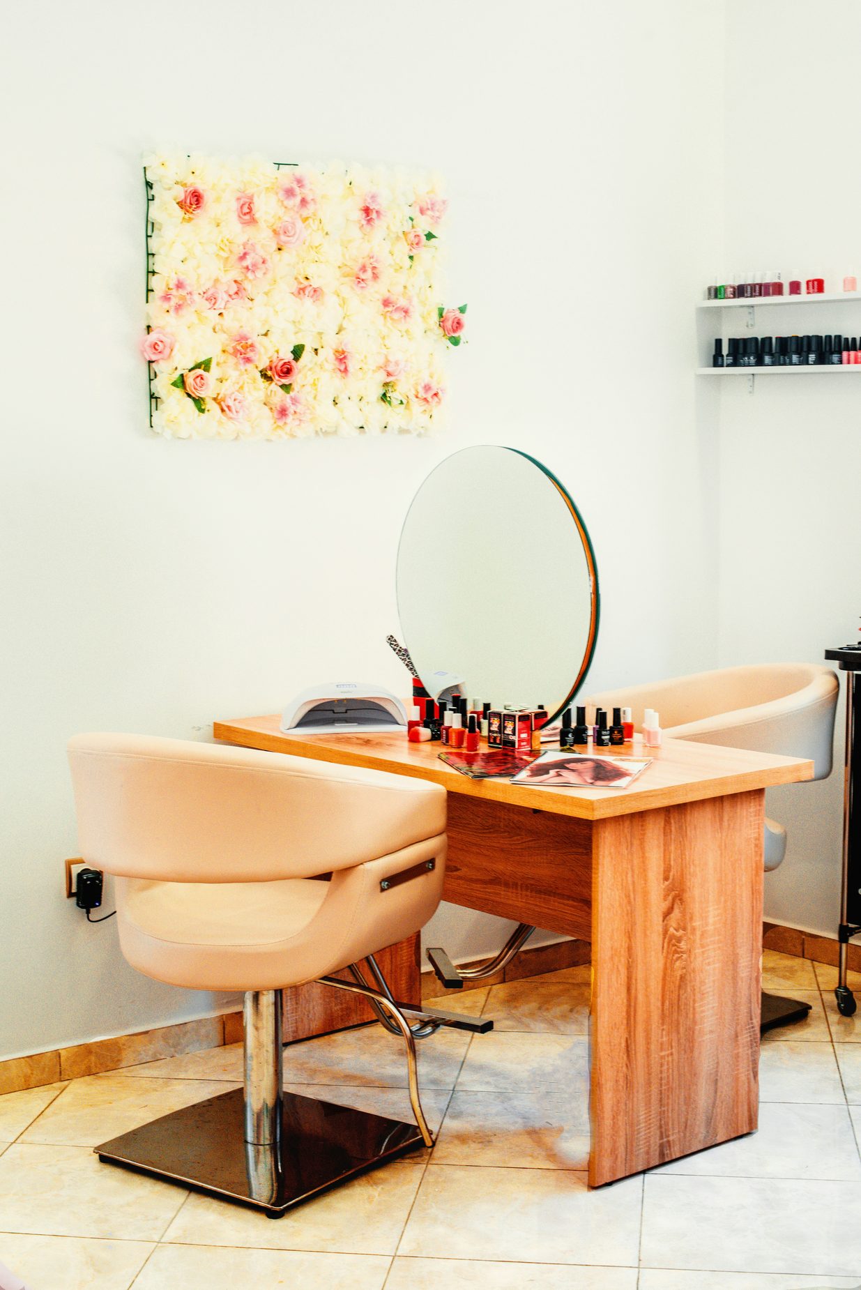 Ingerichte salonwerkplek met houten tafel, ronde spiegel, beige stoelen en een bloemenwand aan de muur