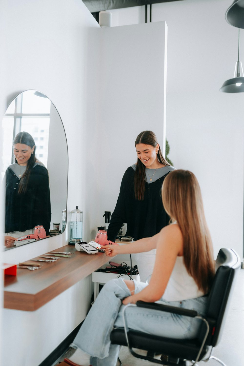 Klant in de salonstoel wordt geholpen door een lachende beauty-ondernemer aan de spiegelbalie