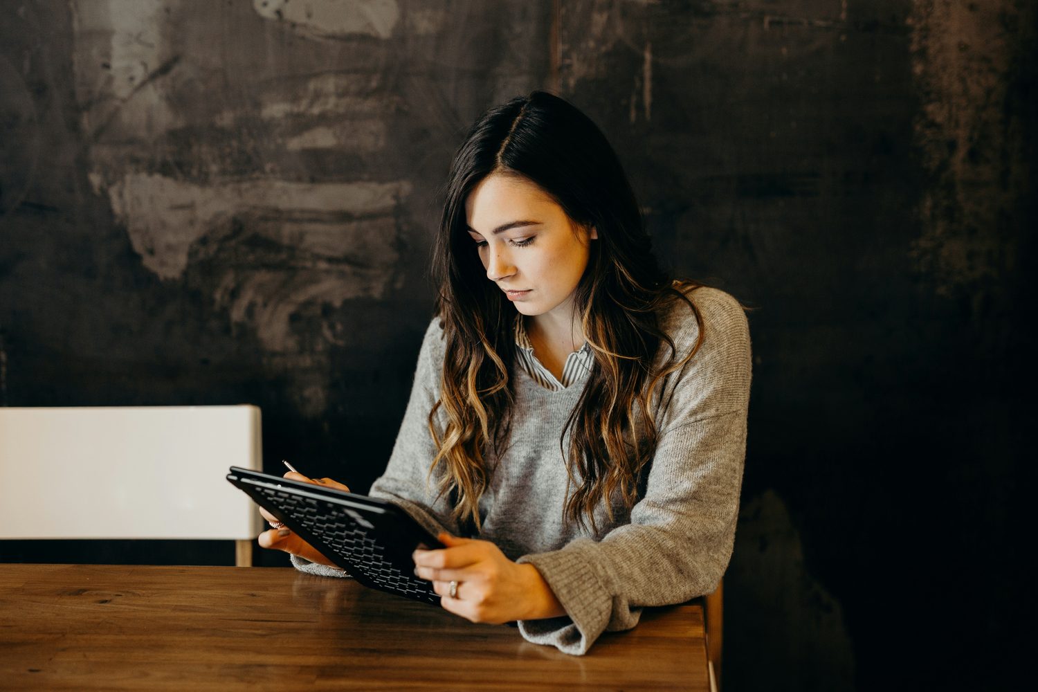 Beauty-ondernemer werkt in haar eentje geconcentreerd op een tablet aan een houten tafel