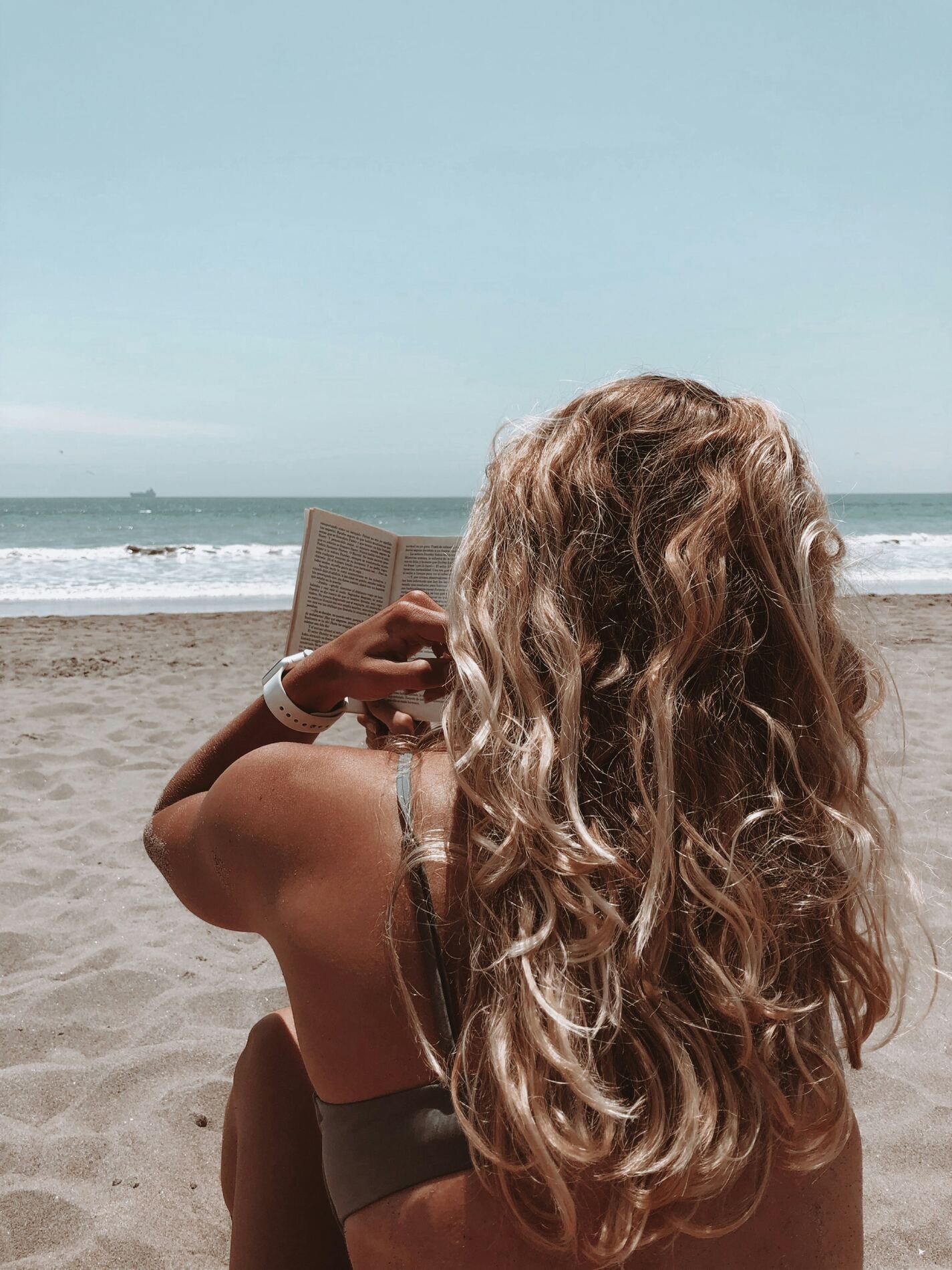 Vrouw op het strand met natuurlijke look en golvend haar, kijkt uit over zee