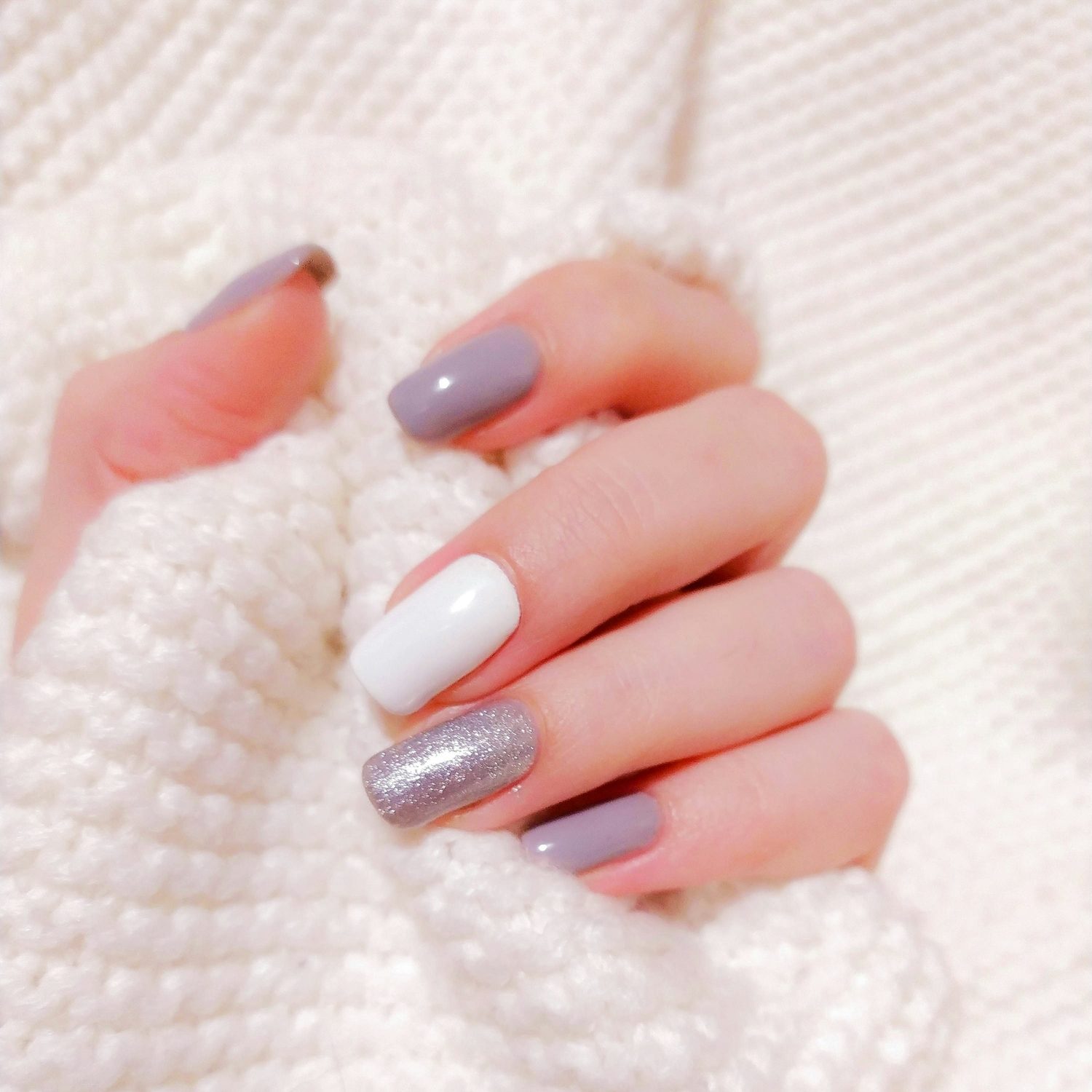 Close-up van een hand met verzorgde nagels in grijs, wit en zilverglitter gellak