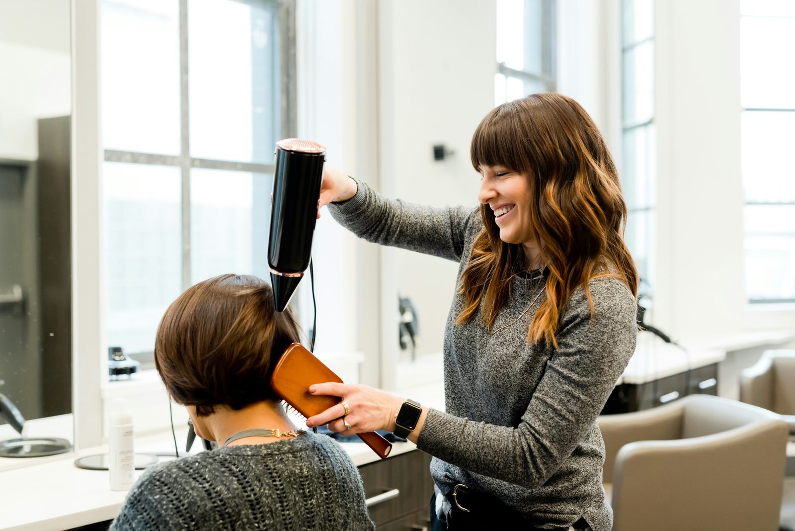 Lachende kapster föhnt het haar van een klant in een lichte salon