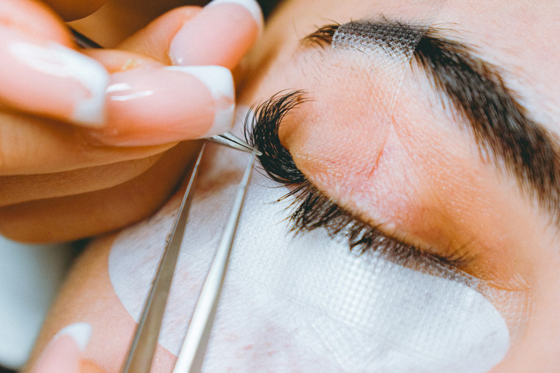 Close-up van een wimperstylist die met een pincet een wimperextension plaatst tijdens een behandeling